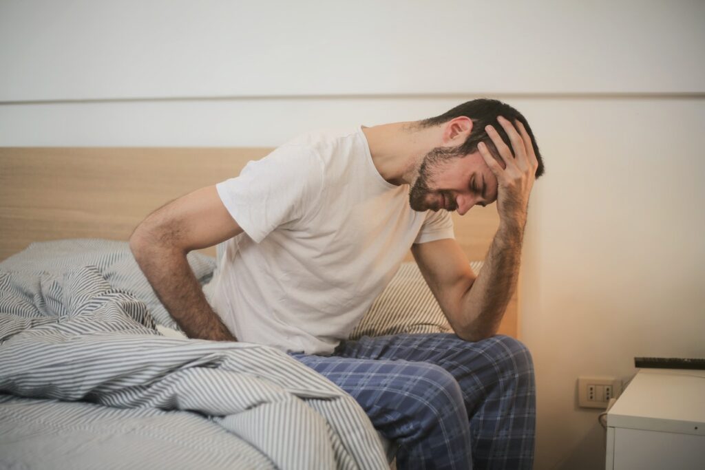 jakie są objawy zatrucia azbestem - mężczyzna w piżamie siedzi na łóżku i trzyma się jedną ręką za głowę