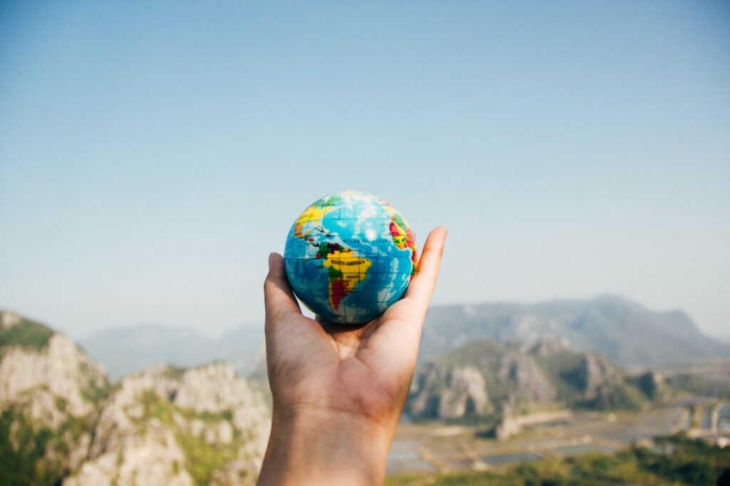 Zdjęcie przedstawia dłoń trzymającą mały globus Ziemi, na tle krajobrazu górskiego. Ma to stanowić ilustrację do bloga o tytule: "Klasyfikacja i rodzaje odpadów".