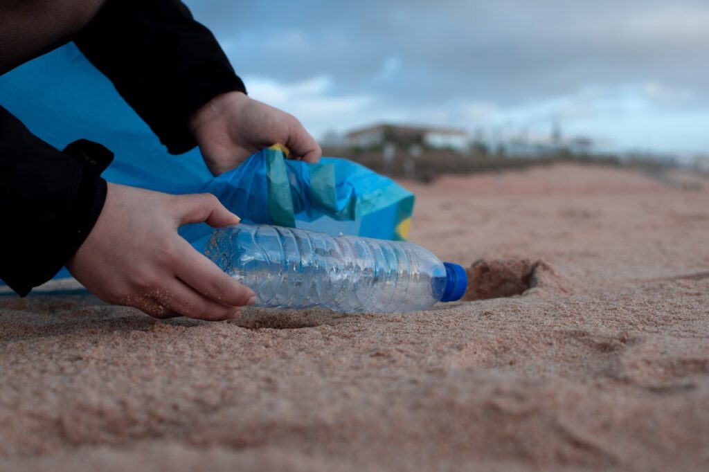 Obrazek przedstawia zdjęcie osoby zbierającej plastikowe odpady z plaży. Ta fotografia ma za zadanie obrazować temat bloga: "Metody unieszkodliwiania odpadów".