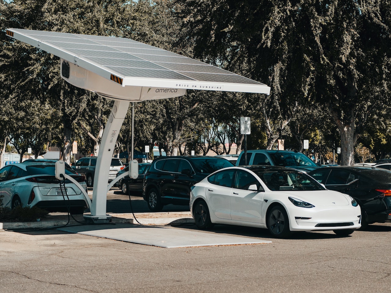 Fotografia przedstawia Teslę - samochód elektryczny, który jest ładowany energią pochodzącą z paneli słonecznych. Zdjęcie jest ilustracją do bloga o tytule: "Jak dbać o ekologię i środowisko naturalne?".