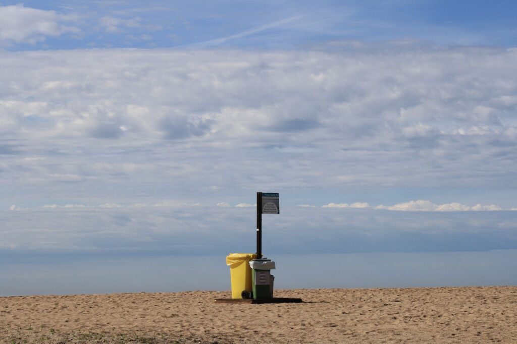 Fotografia przedstawia dwa kubły na odpady na plaży na tle niebieskiego nieba. Jest to ilustracja do bloga o tytule: "Mechaniczno-biologiczne przetwarzanie odpadów - na czym polega?".