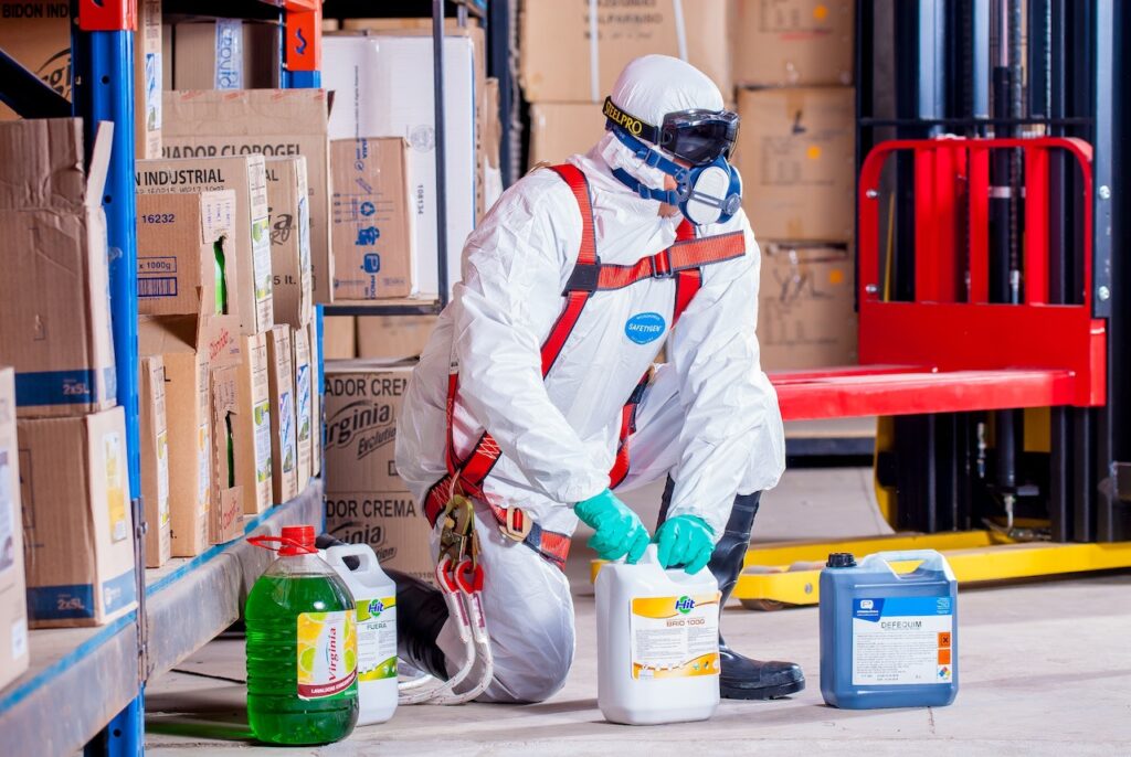 Fotografia przedstawia osobę w białym uniformie ochronnym, która zajmuje się chemikaliami w butelkach. Jest to ilustracja do bloga o tytule: "Metody unieszkodliwiania odpadów".