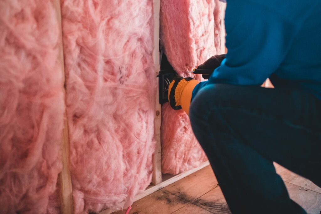 Fotografia przedstawia mężczyznę montującego izolację z różowej wełny mineralnej. Jest to ilustracja do bloga o tytule: "Utylizacja wełny mineralnej".